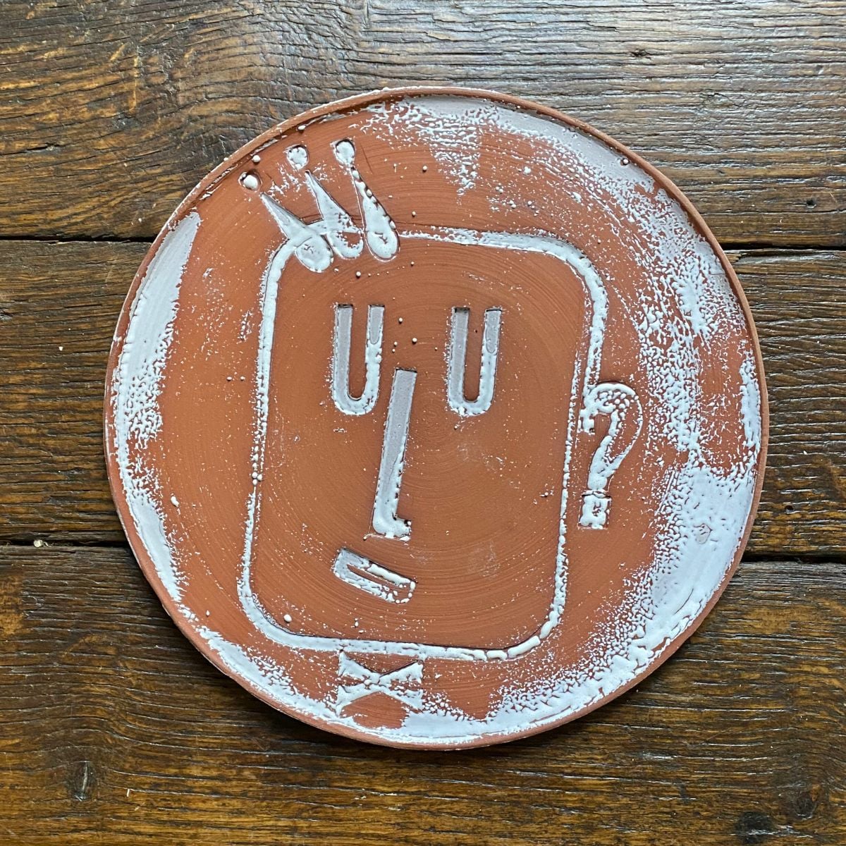 Round, decorative plate with face made from letterpress block impressions on a wooden floor