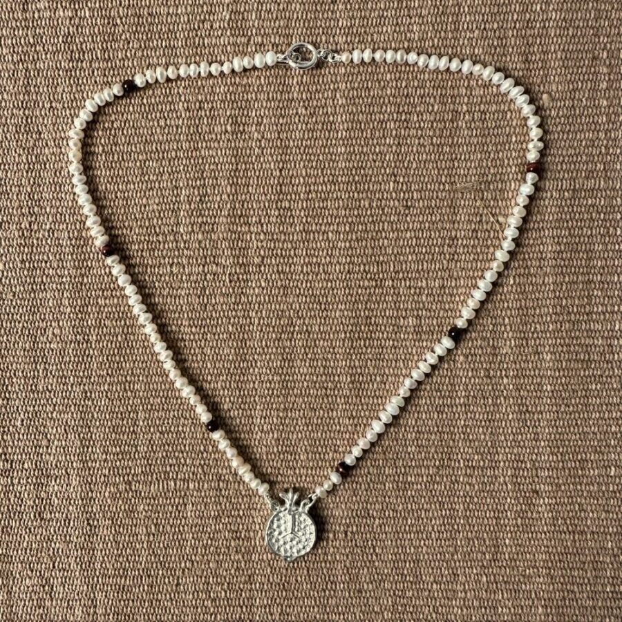 A seed pearl and red tigers eye necklace with a cast silver pomegranate pendant. Clare de la Torre.